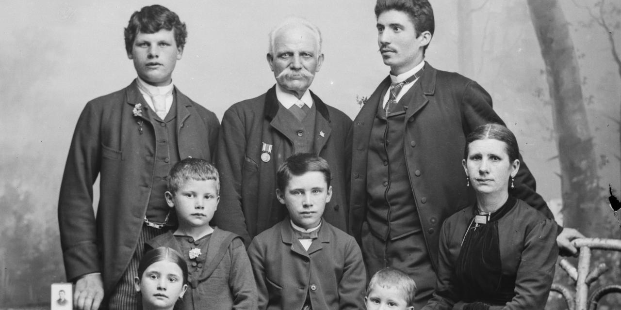 Portrætfotografi af en familie med to mænd, en ældre herre, en kvinde og fire børn.