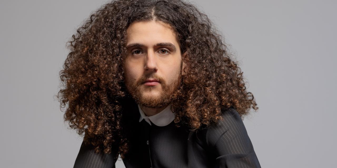 Billede af Elias Sadaq i jakkesæt på en stol.