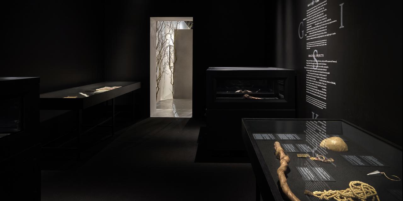 Et mørkt lokal i udstillingen, hvor forskellige genstande ligger i montrer.