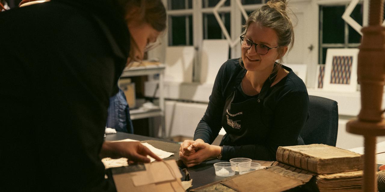 Medarbejder sidder og taler med en gæst om en bog, gæsten har i hånden.