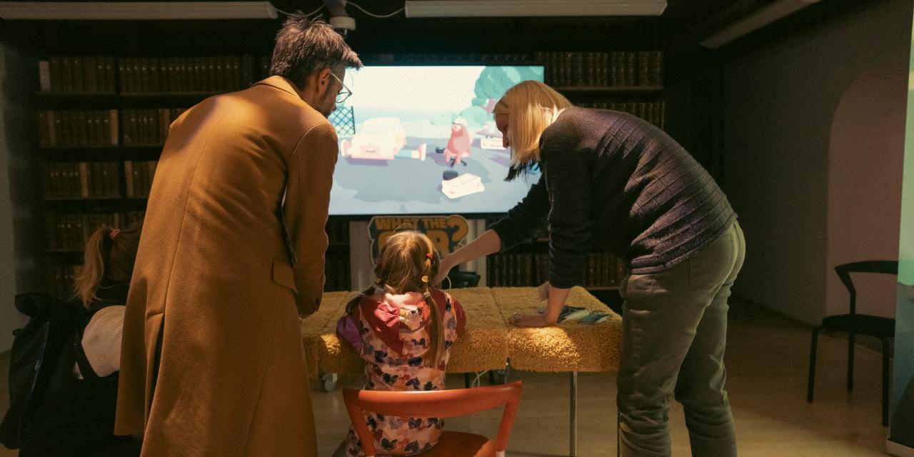 Et barn sidder og spiller et computerspil, imens forældrene kigger på