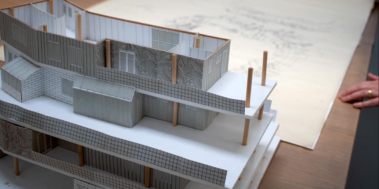 Miniature model af et hus i fire etager. Tegninger i baggrunden.