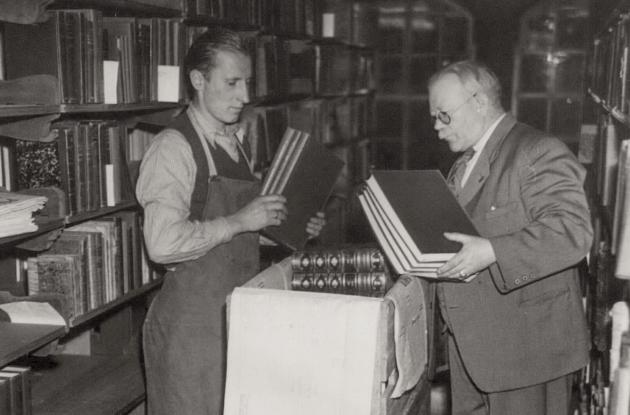 Library staff among books and bookshelves. Older