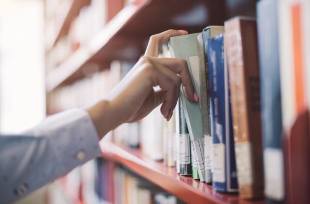 Hand takes book from bookshelf