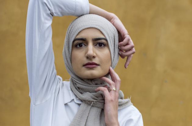 Digteren Naiha Khiljee poserer i hvidt foran en okkergul væg.