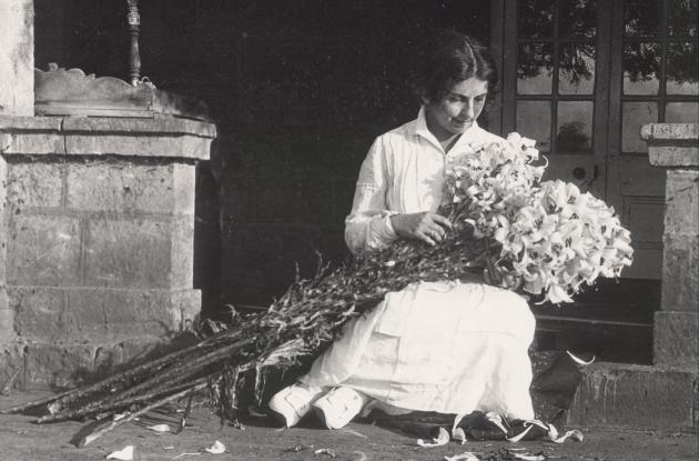 Karen Blixen is sitting on a step with a large bouquet of lilies