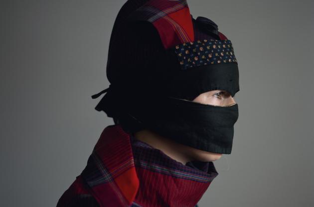 A woman is sitting in profile with her head covered by a strude mask