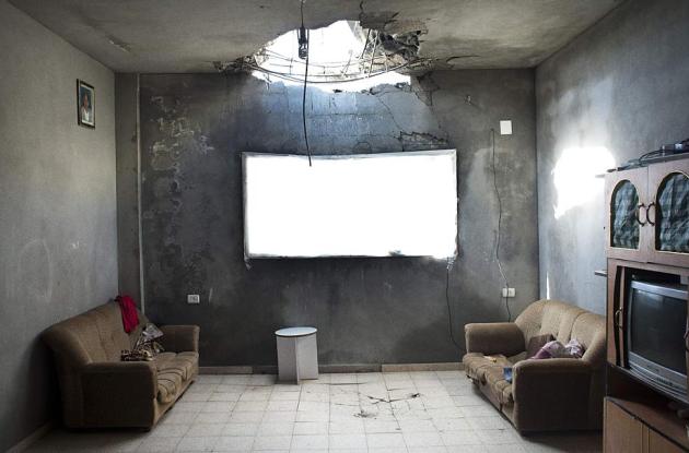 Stue med to brune sofaer og et stort hul i loftet efter bombe.
