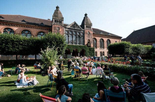 Det Kgl. Bibliotek's old building in the background - in the foreground, guests sit on the grass and listen