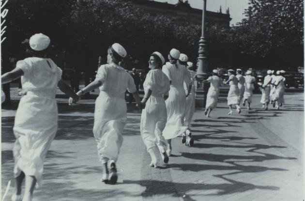 Studiner danser rundt i rundkreds med hvide kjole og studenterhuer