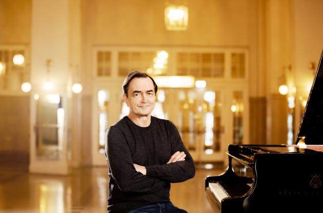 Photo by pianist Pierre-Laurent Aimard at a grand piano in golden light