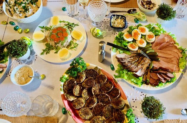 Fyldt påskefrokost bord med æggeretter, udskåret kød, karse og æggedekorationer.