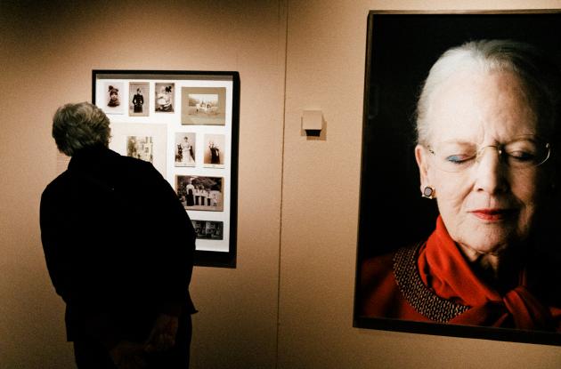 Gæst i udstilling kigger på portrætfotos - et stor portræt af dronningen ses ved siden af