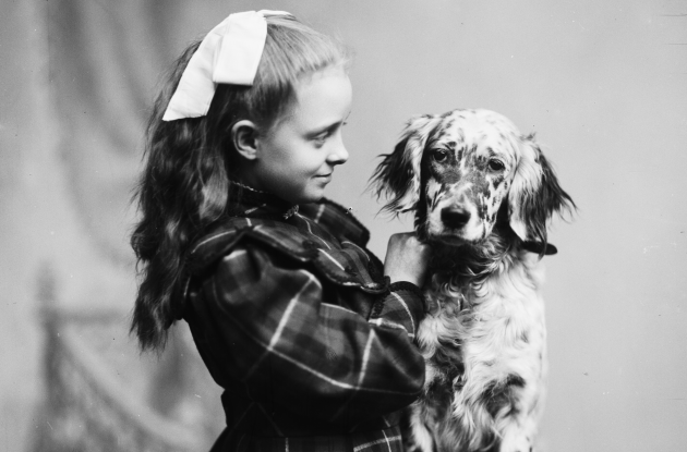 Fotografi af pige med kjole og sløjfe, der står med en hund