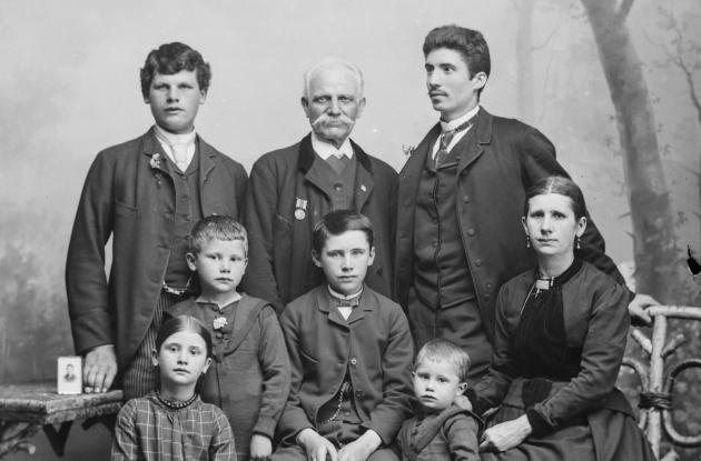 Portrætfotografi af en familie med to mænd, en ældre herre, en kvinde og fire børn.