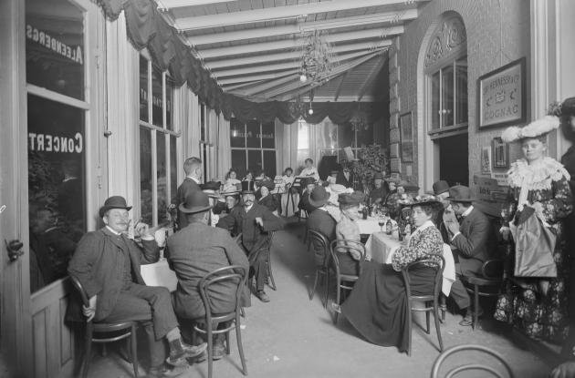 A pub where people sit neatly dressed and wearing hats around tables