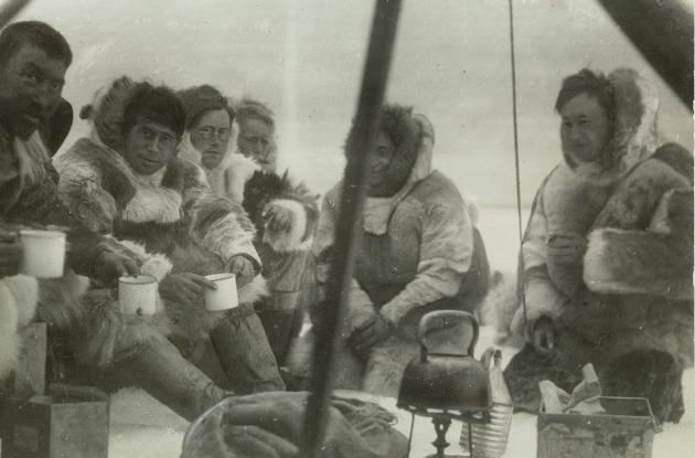 Photograph of Knud Rasmussen and the members of the expedition, sitting closely in a tent with warm fur clothing on.
