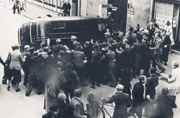 Photograph of a crowd overturning a prison van in the street.