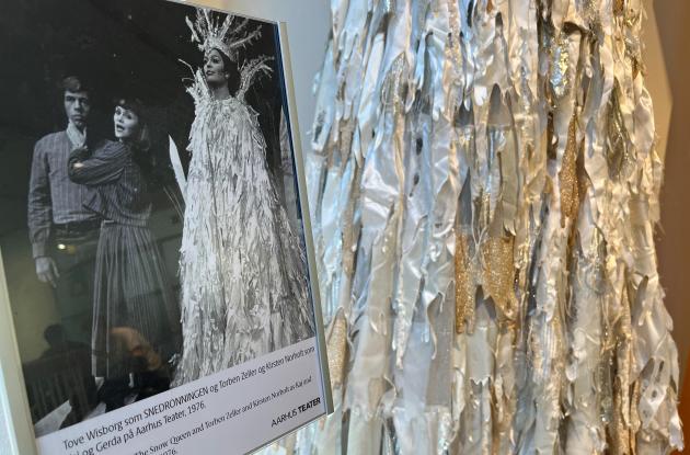 Et skilt, med et billede af teaterforestillingen Snedronningen 1976, med Tove Wisborg som snedronningen iført en kjole, som man ser en smule af bag ved skiltet. 