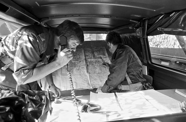 En kommandostation fra 2. Sjællandske Brigade. To mænd står over et kort og dokumenter. Den ene har en telefon mod øret.