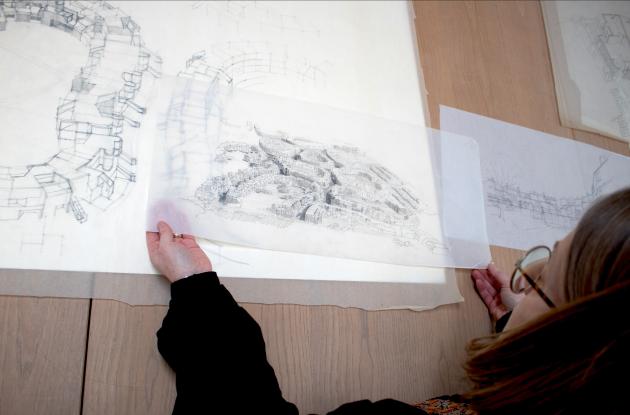 Billede af en kvinde, der holder en arkitekturtegning. Der er andre tegninger i baggrunden.