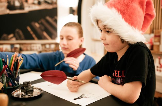 Children in Santa hats writing with quills
