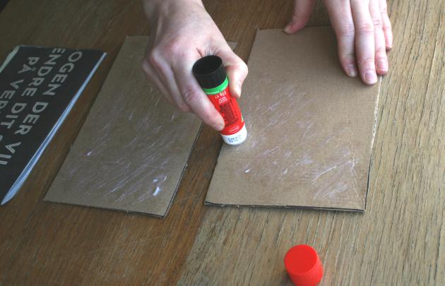 A hand glues a piece of cardboard