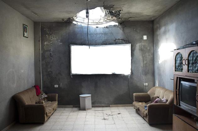 Stue med to brune sofaer og et stort hul i loftet efter bombe.