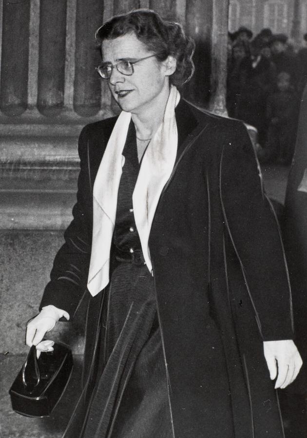 Bodil Koch walking in a long coat carrying a handbag.