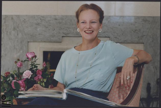 Farvebillede af Dronning Margrethe II, der sidder med en bog i skødet.