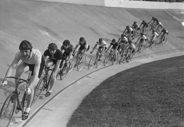 Men ride bikes in a row on a bicycle track