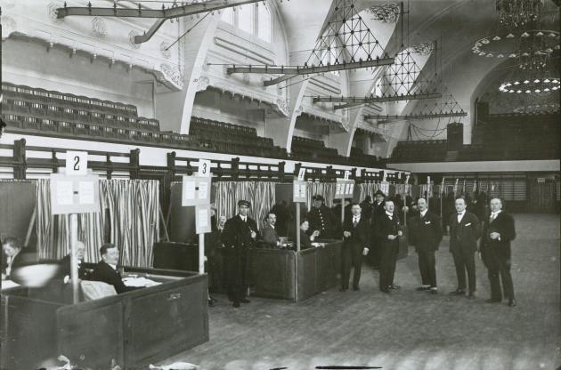 Mænd i jakkesæt står i afstemningslokale i gymnastiksal 2. dec. 1926