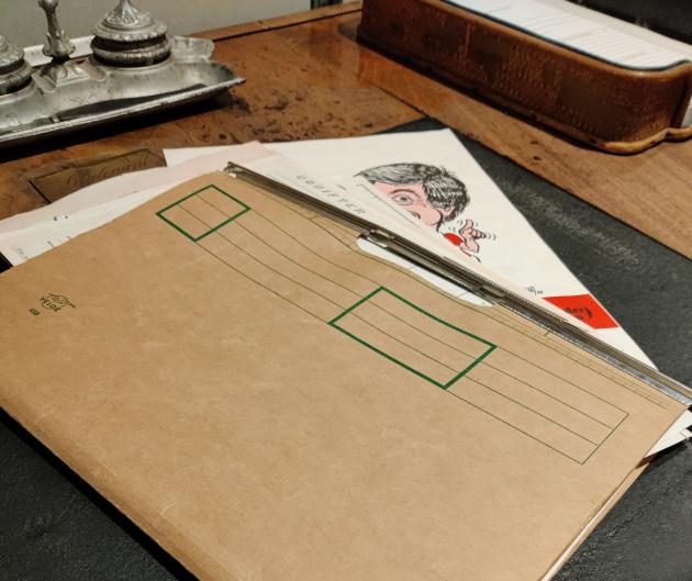 En brun mappe ligger på et skrivebord. En fodboldplakat stikker ud fra mappen.