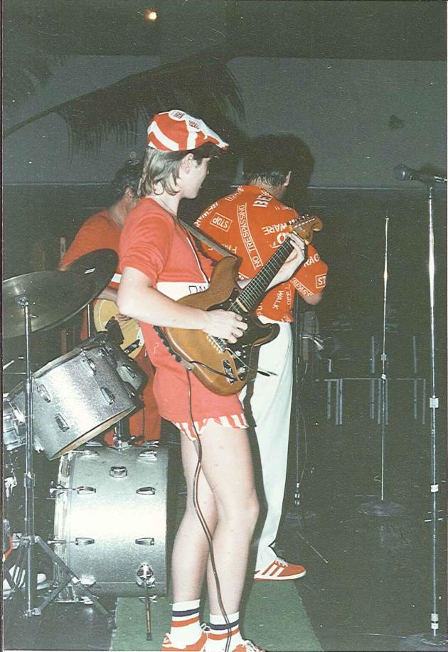Man in shorts plays electric guitar in band.