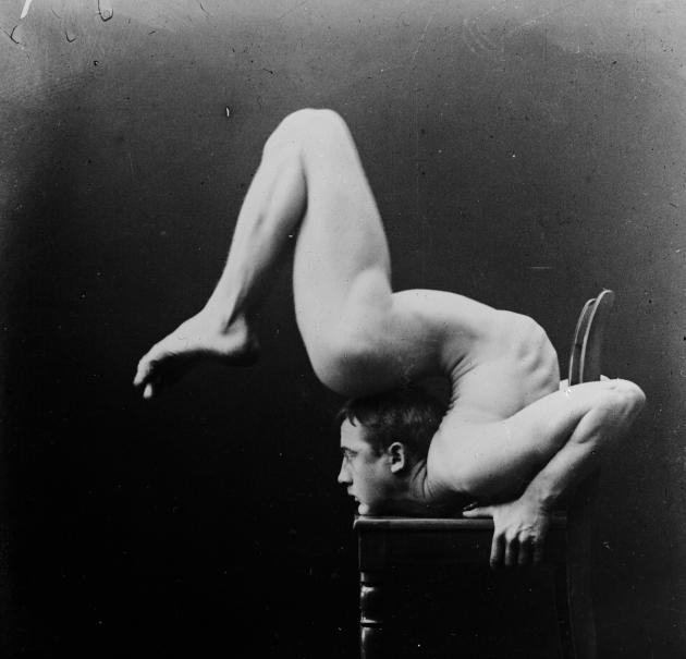 Photograph of a naked man in a highly acrobatic position on a chair.