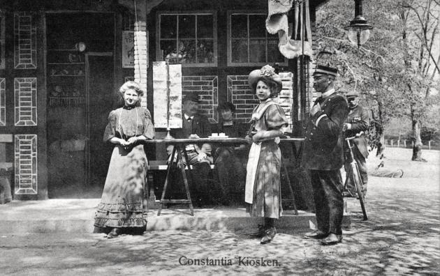 Postkortbillede af en gruppe mennesker foran en kiosk.