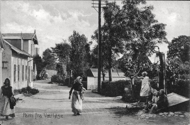 Billede af en vej, hvorpå der går to kvinder. Den ene kvinde ser ud til at tale med en anden kvinde, der står ved siden af vejen.