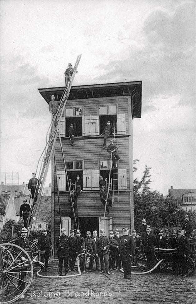 Brandstation i tre etager med poserende brandmænd med stier, vandslanger og reb.