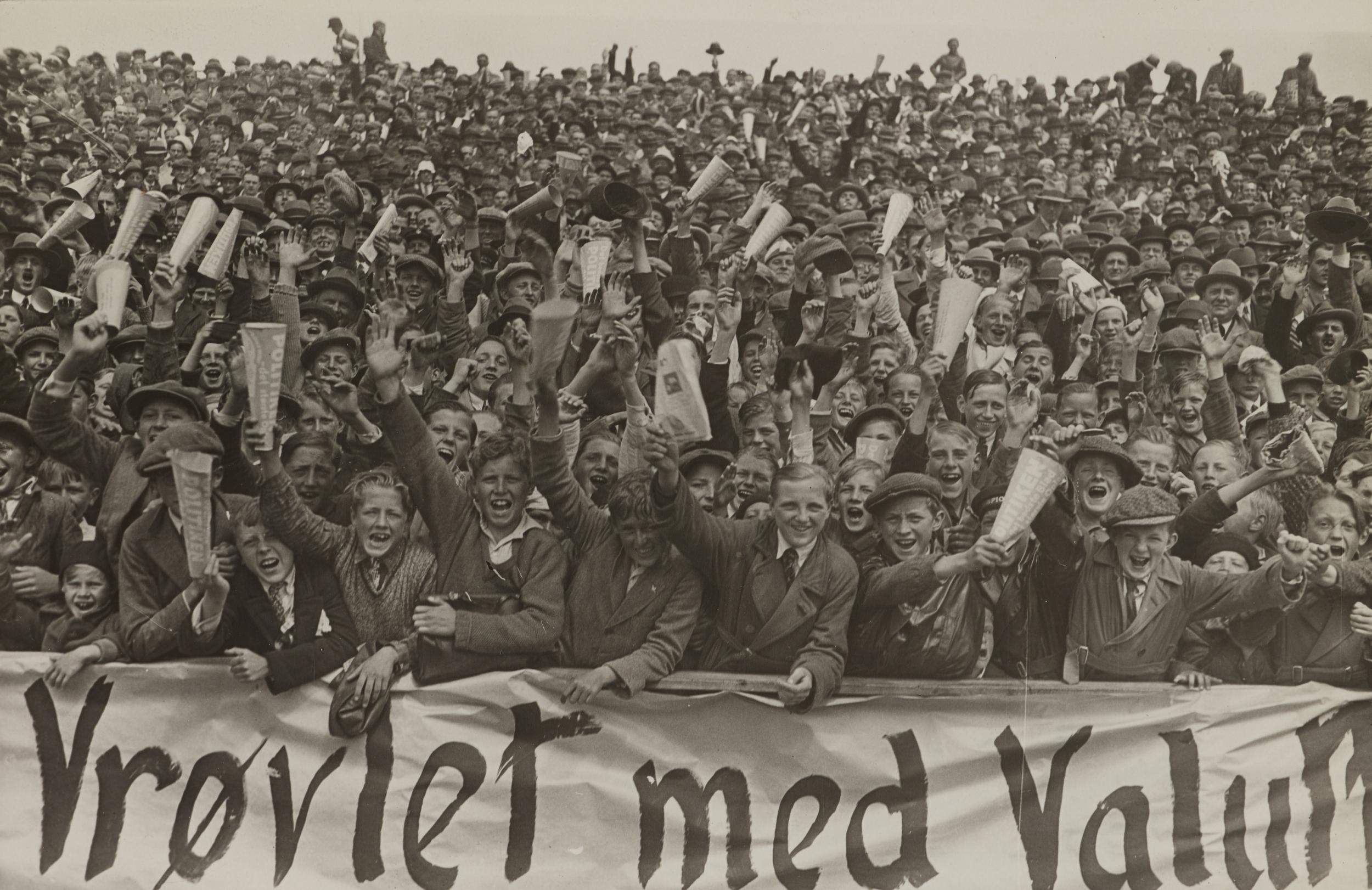 Stor gruppe af mennesker smiler til kameraet og løfter avisen Politiken i vejret