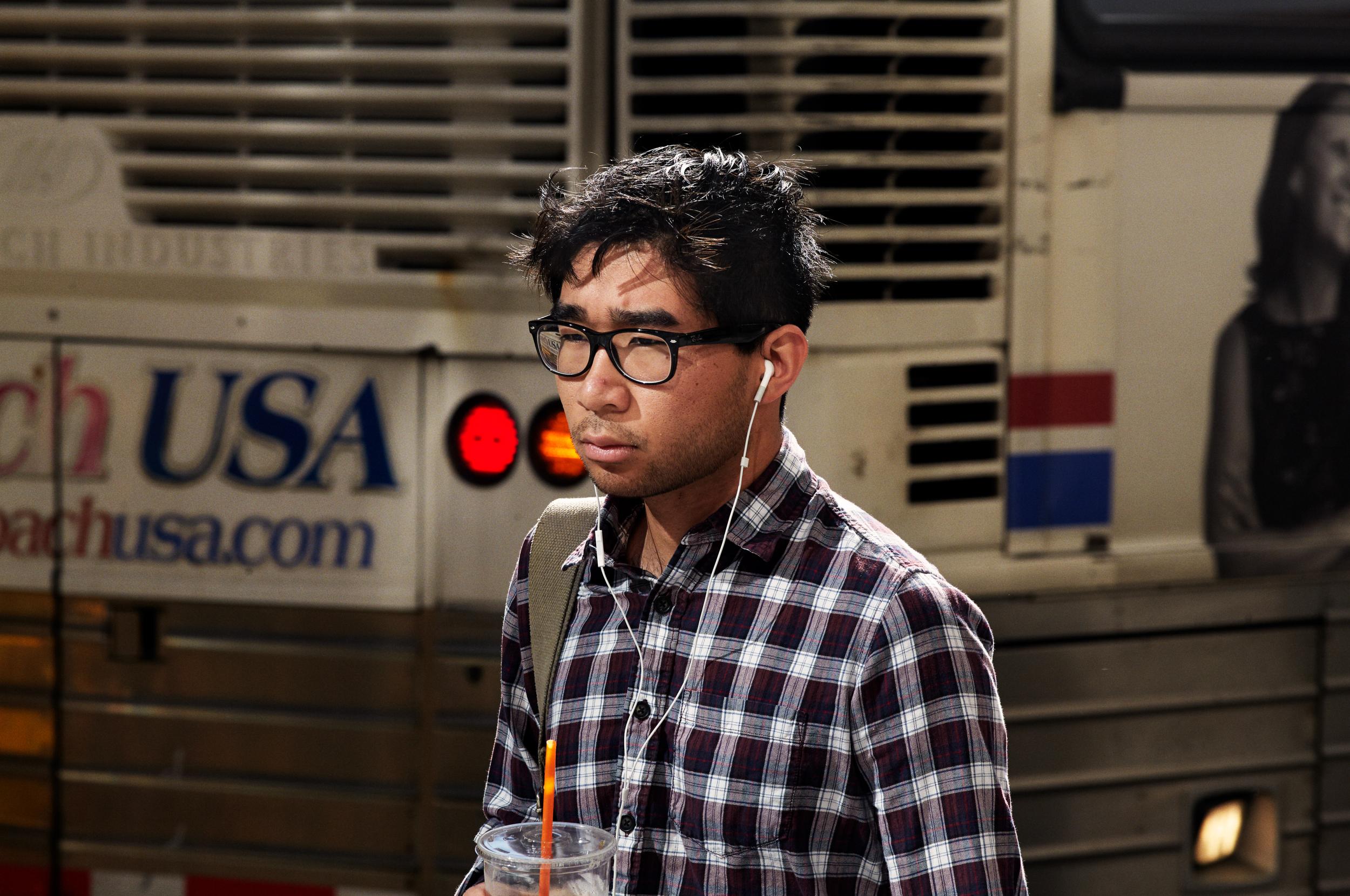 Mand med briller, høretelefoner og kaffe går på gade