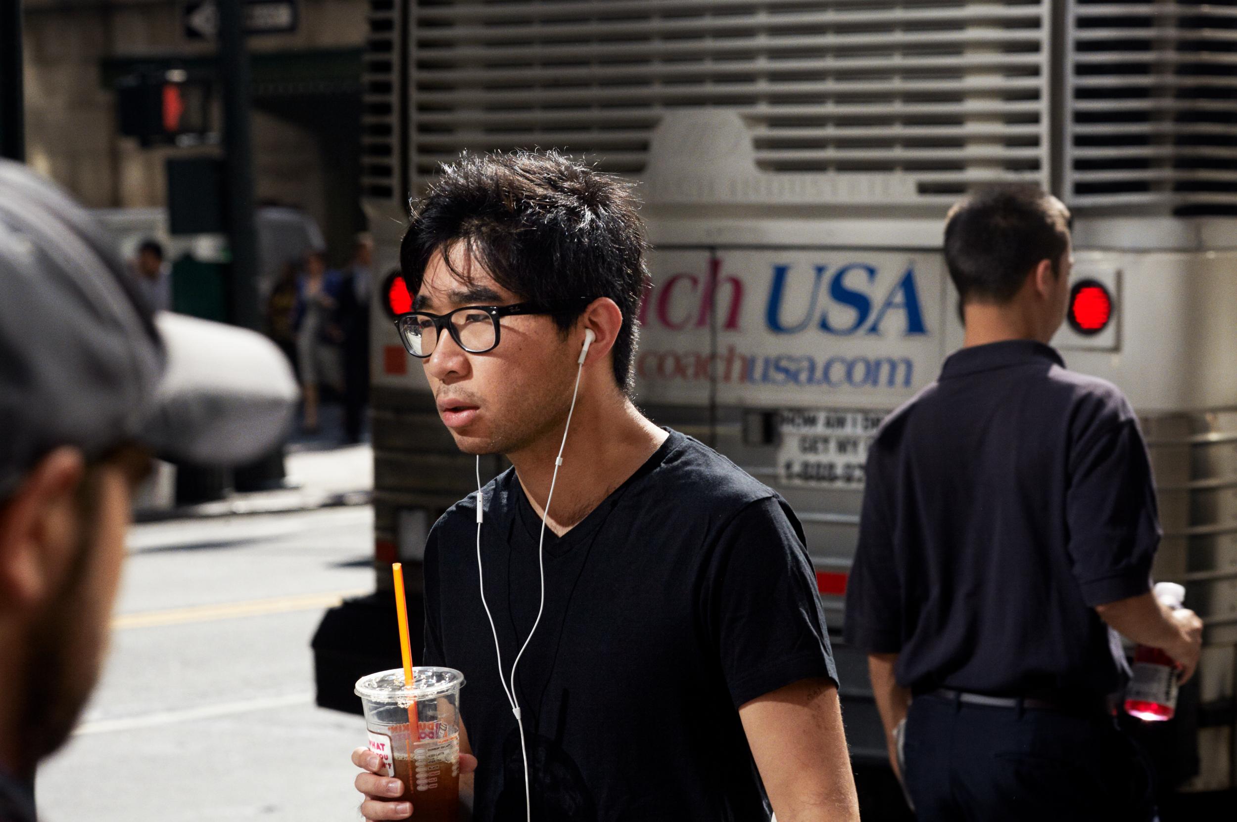 Mand med høretelefoner og kaffekop går på gade