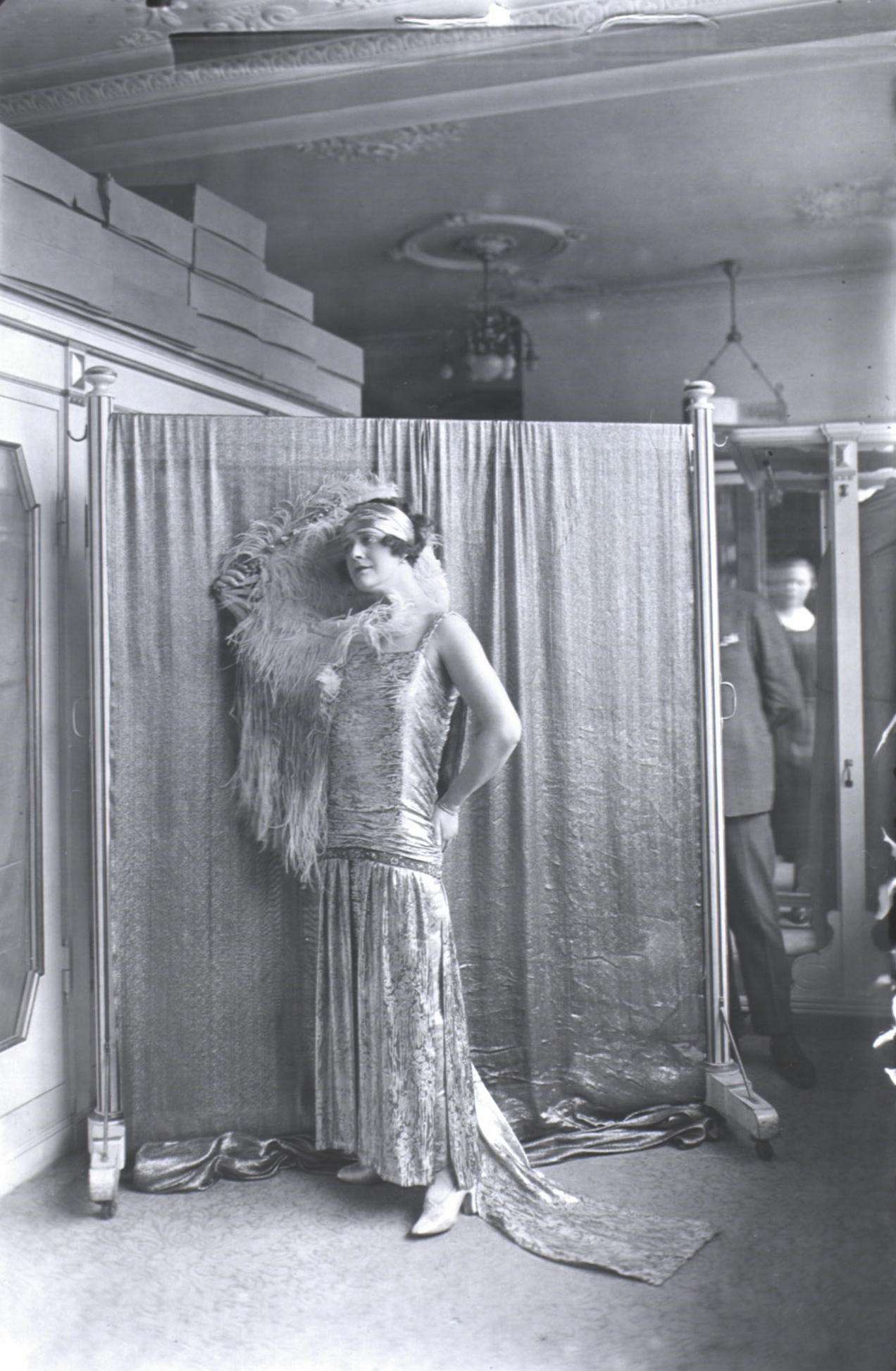 Kvinde poserer foran klæde iført lang kjole og fjer.