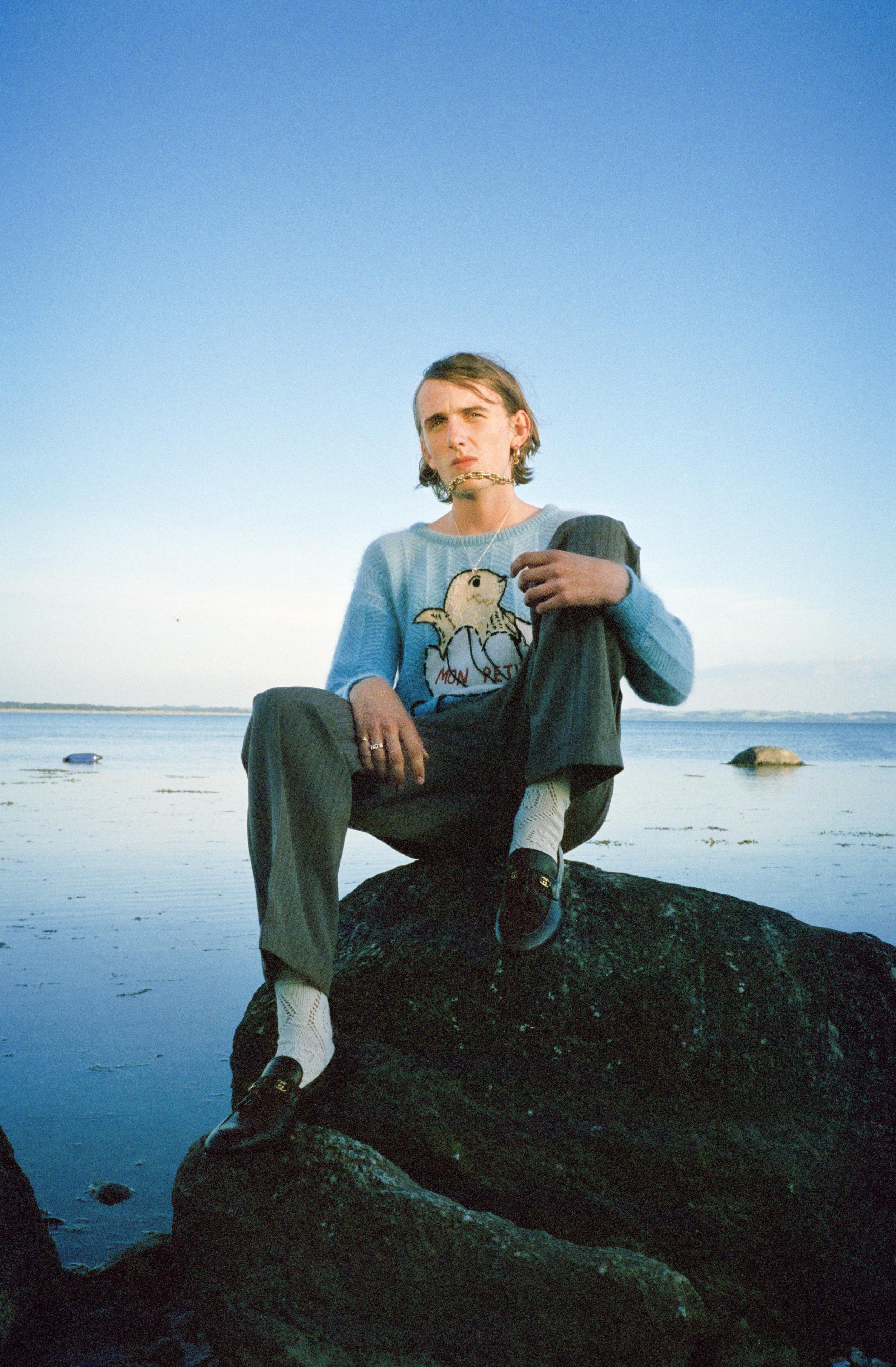 Ung mand sidder på en sten i vandkanten