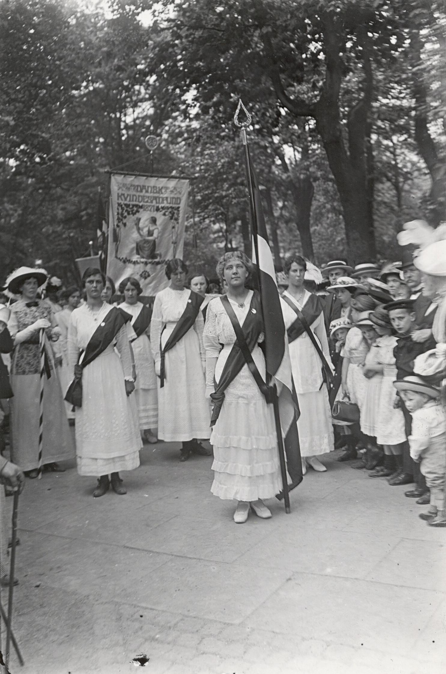 Kvinder i hvidt går i procession med en fane.