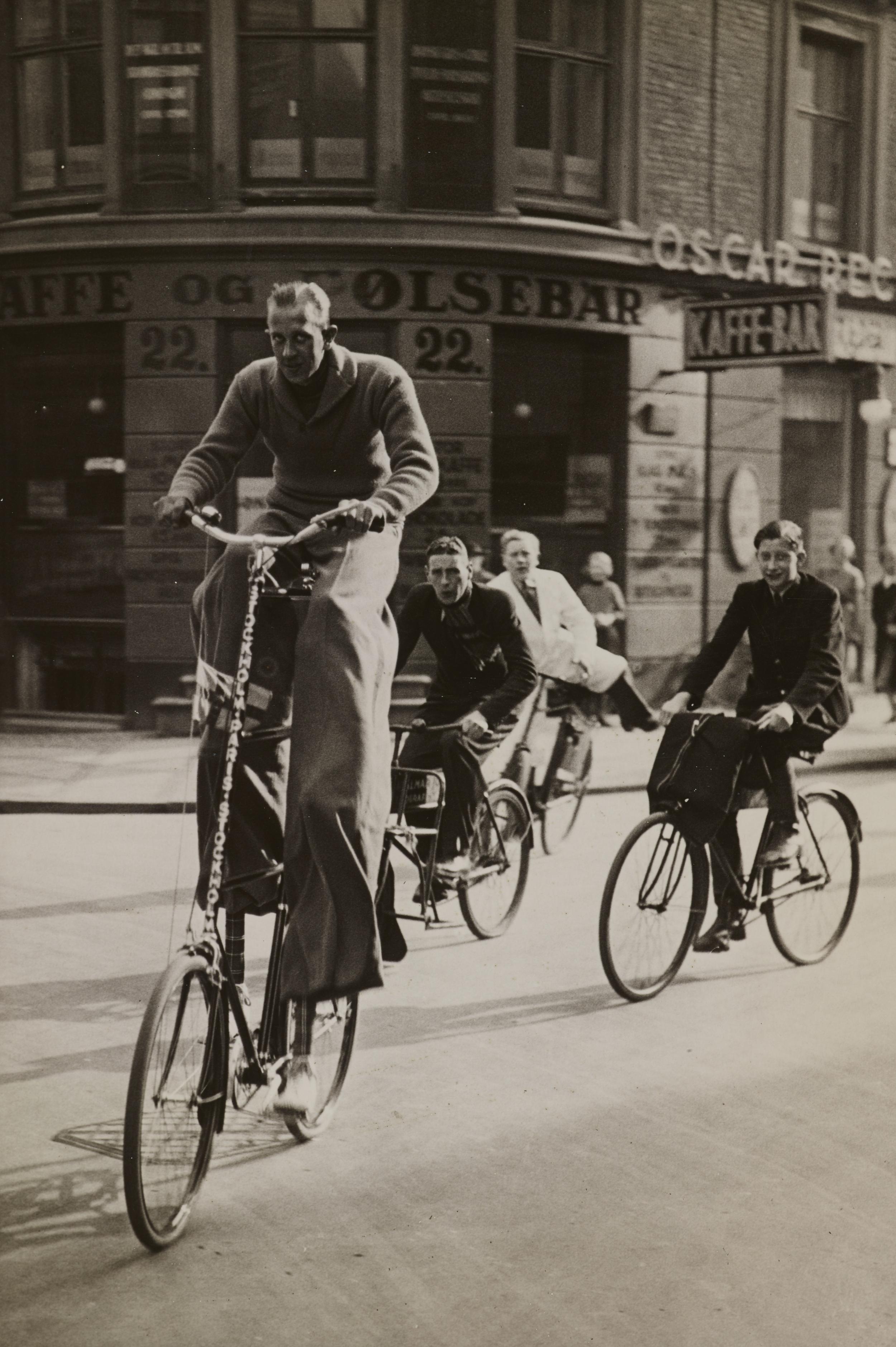 Tre mænd på cykler. Den forreste mand cykler på en væltepeter.
