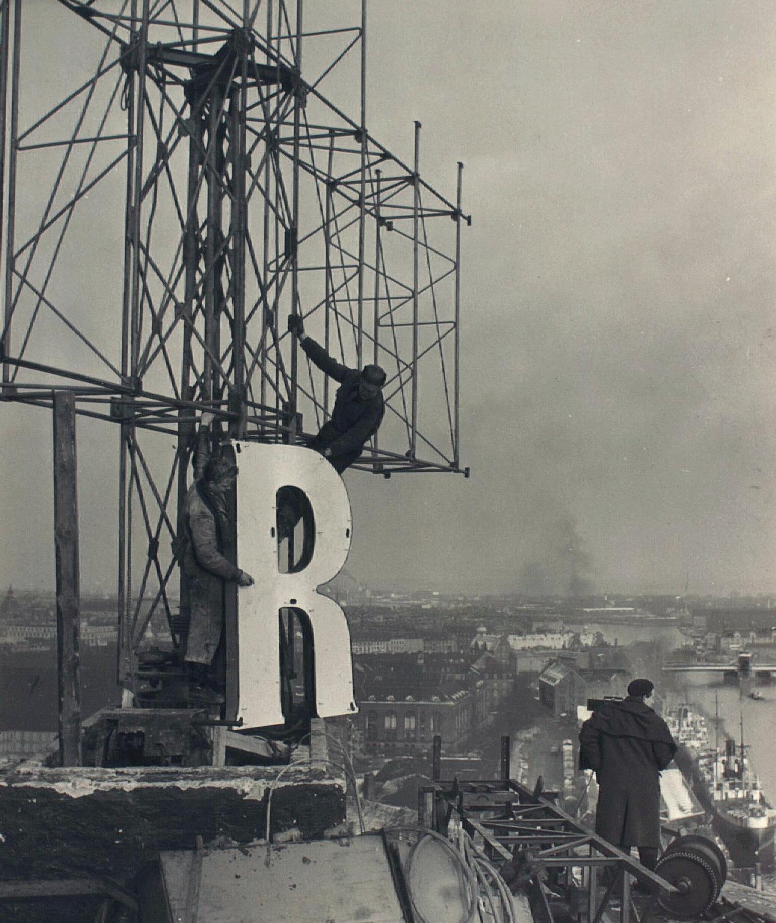 En mand kravler på et stillads for at sætte et stort R-bogstav op.