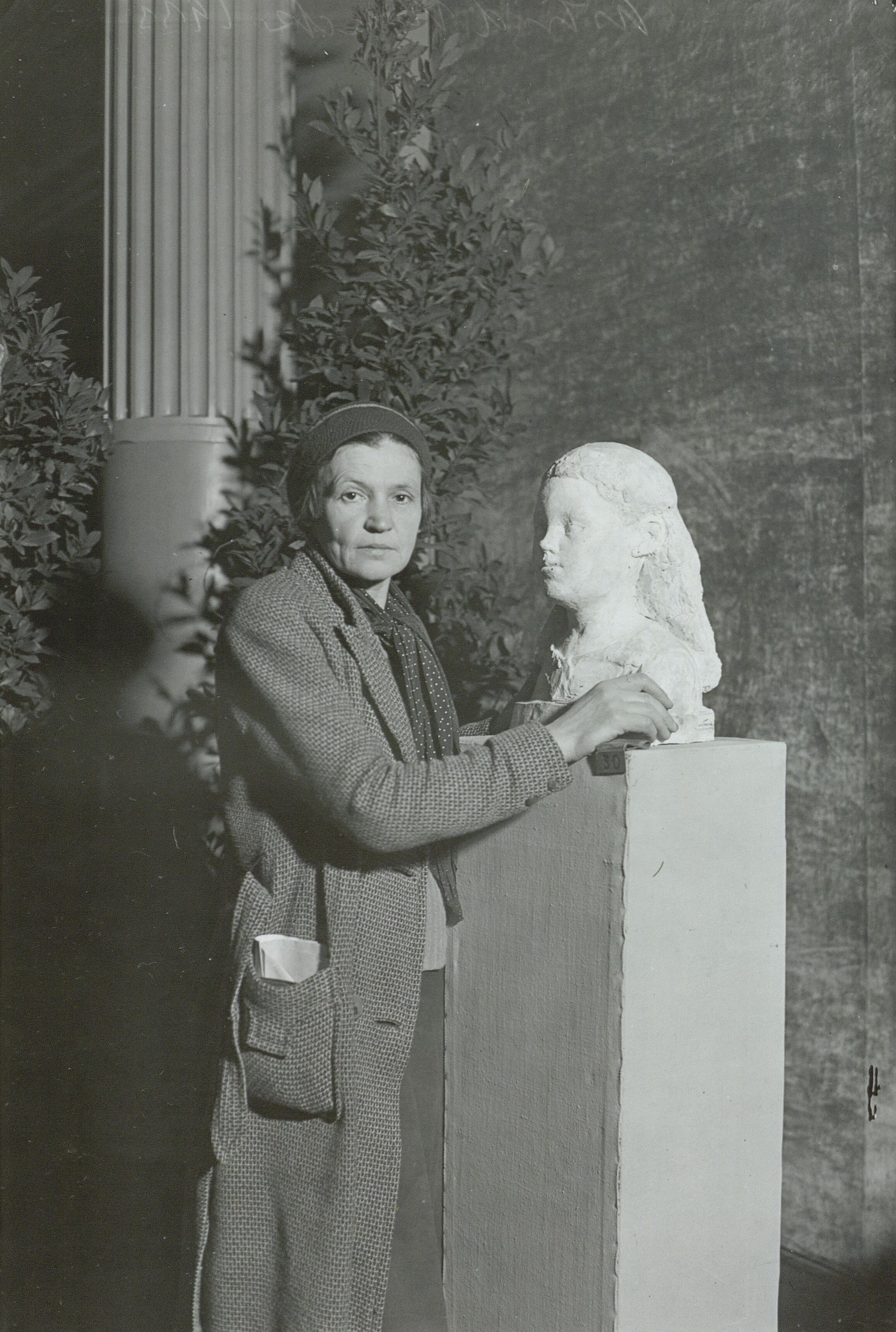 Billedhuggeren Astrid Noack står ved siden af en statur af en kvindes ansigt. Noack bærer en frakke og hue.