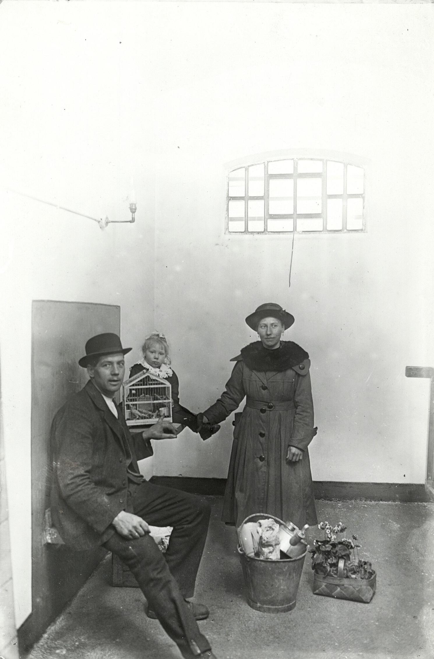 En mand, en dame og et barn er i et tomt fængselslokale med højt til loftet. På jorden er deres ejendele.