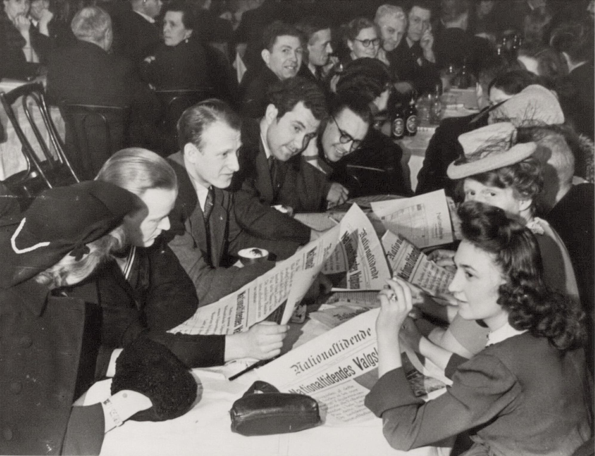 Men and women sit at a long table with the newspaper National Tidende