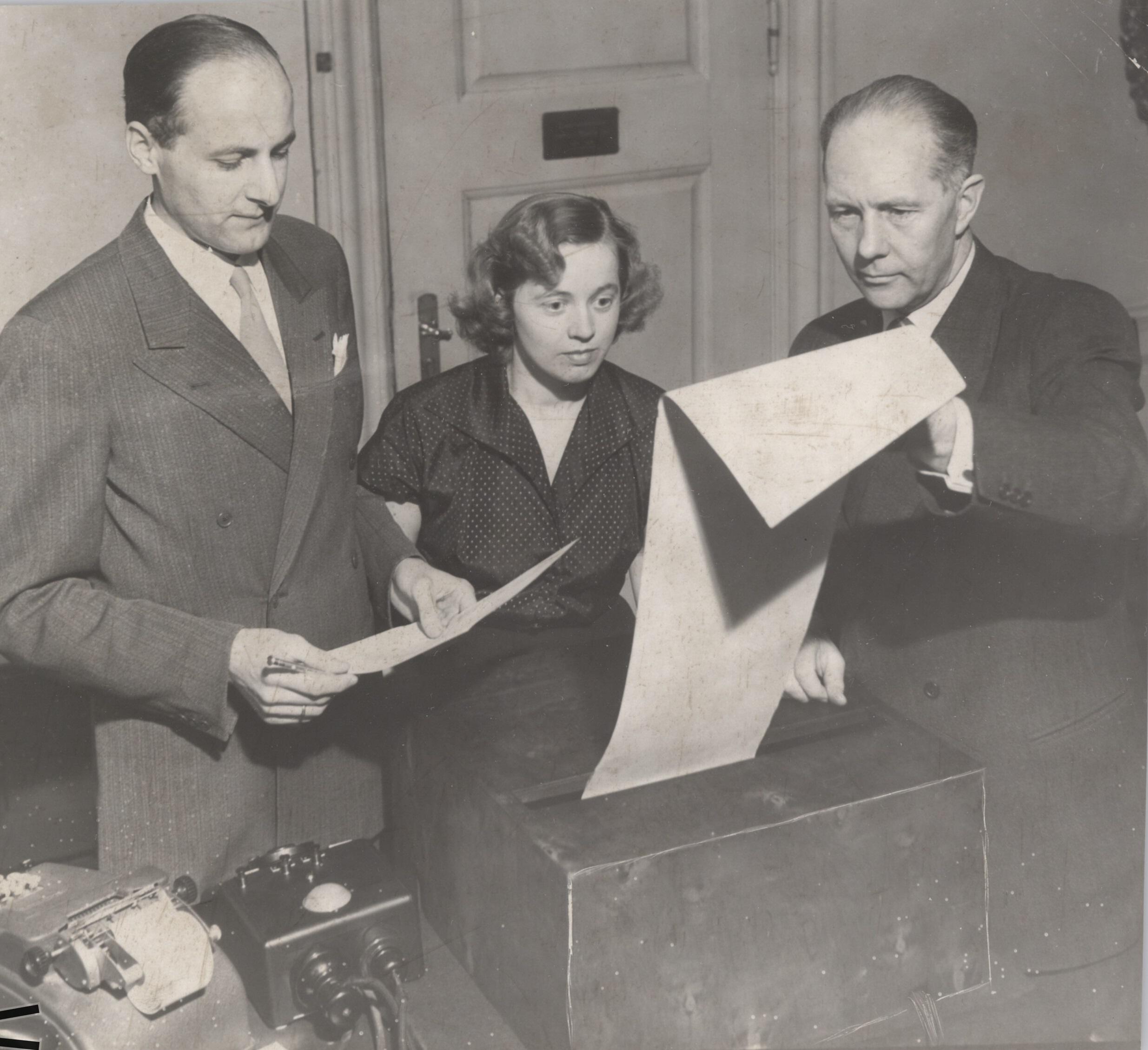A woman and two men look at the election results, which arrive on teleprinter at the Ministry of the Interior's Election Office